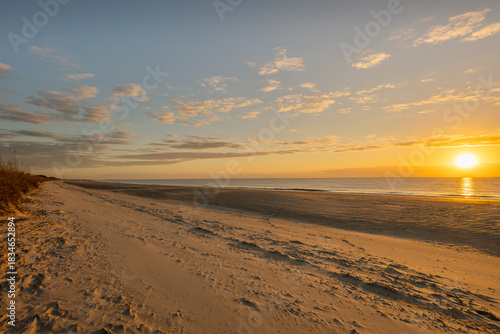 Sunset on a sandy beach with calm waves and distant clouds in the sky near the water