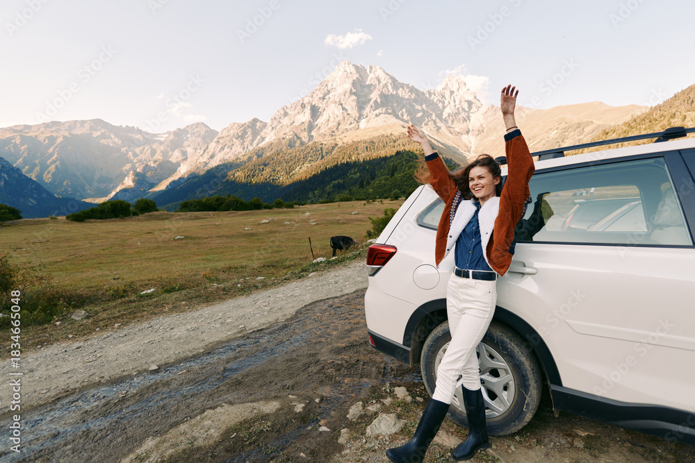 Fototapeta premium Woman by car in mountains, travel and nature road in countryside with raised arms, smiling and enjoying adventure and scenic view near parked SUV on gravel path.