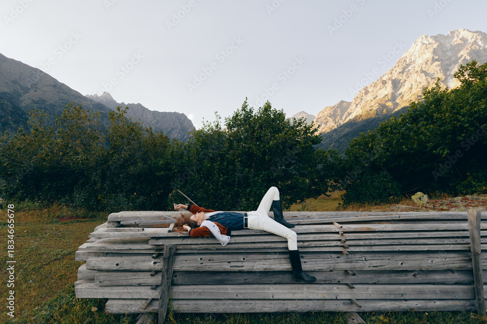 Fototapeta premium woman lying on wooden bench in mountain nature scene with forest backdrop and meadow, relaxed outdoors lifestyle portrait, casual fashion and peaceful resting in scenic travel escape