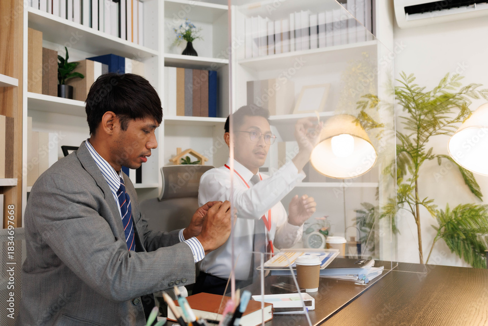Obraz premium Two male employees in suits are designing a business plan, discussing various plans in their office, and one is drawing on a whiteboard. The scene looks cheerful and fun.