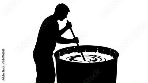 Silhouette of a person stirring a large container with a long stick