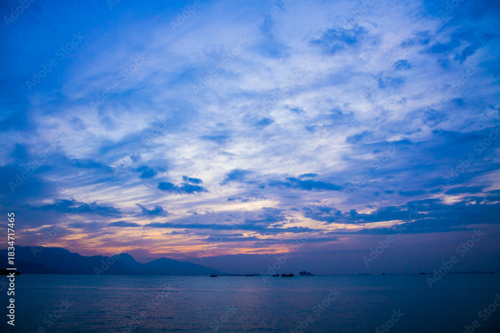 Obraz premium A tranquil coastal scene at dusk with boats, mountains, and a sky filled with blue, purple, and orange hues.