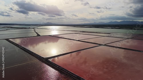 Aerial drone view of colorful salt ponds near Santa Pola, Spain, with pink and green water reflecting clouds and sunlight over the Mediterranean coast.