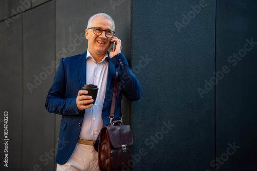 Mature businessman smiling talking on smartphone drinking coffee