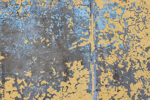 Yellow peeling paint on the wall. Old concrete wall with cracked flaking paint. Weathered rough painted surface with patterns of cracks and peeling. High resolution texture for background and design.