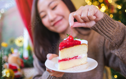 Closeup image of a woman holding and eating a piece of cherry cake in Christmas holidays