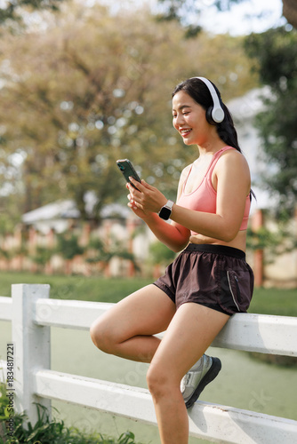 Young asian woman relaxing in park using smartphone and headphones