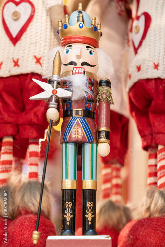 A traditional Nutcracker figure dressed as a royal soldier stands with a sword against a red festive backdrop.