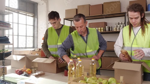 Diverse team of volunteers packing donate food and clothes into boxes, humanitarian aid