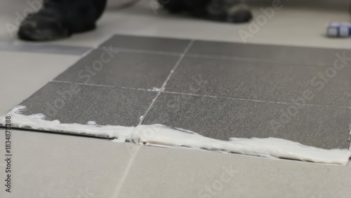 Professional tiler applying fresh white grout between grey ceramic floor tiles.