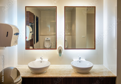 Modern Public Restroom Interior with Dual Vessel Sinks and Backlit Mirrors. Clean washroom featuring white vessel sinks on a marble countertop, large wooden-framed mirrors, and backlit wall lighting.