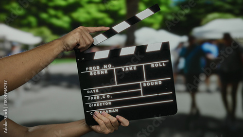 Bild auf Leinwand Man holding clapperboard in outdoor market with blurred people in background on a sunny day