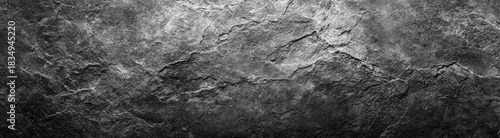 Close-up of dark grey, textured stone surface with natural cracks and subtle variations in light and shadow