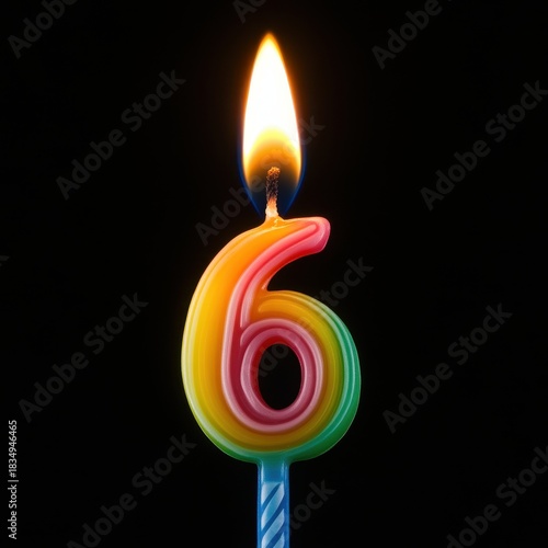 A candle shaped like the number six is lit against a black background during a birthday event