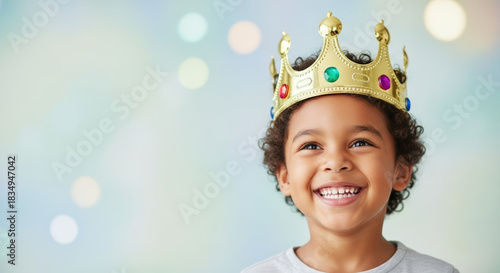 Adorable child celebrates Father's Day with bright smile and wears golden crown to honor parent. Father's Day celebrations bring joy as child looks up against blurred bokeh background,