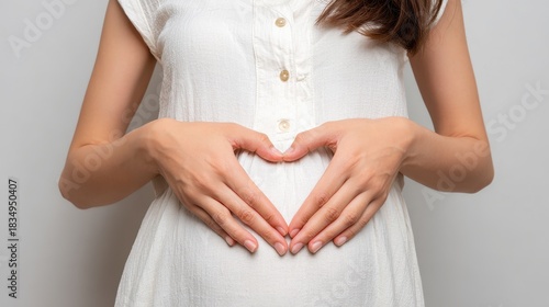 Wallpaper Mural Pregnant woman making a heart shape with hands on her belly while wearing a light, casual dress in a neutral setting Torontodigital.ca