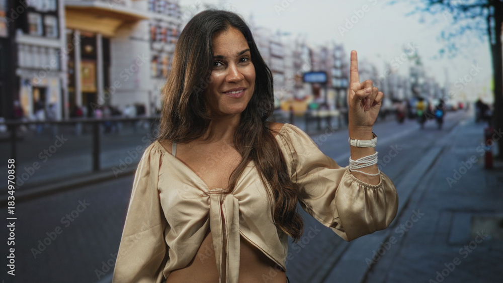 Fototapeta premium Woman points finger upward on street showing bare midriff and tied blouse; confidence spontaneity adventure.