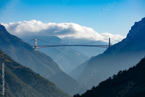 A majestic suspension bridge stretches across a deep, verdant valley between towering mountains under a blue sky