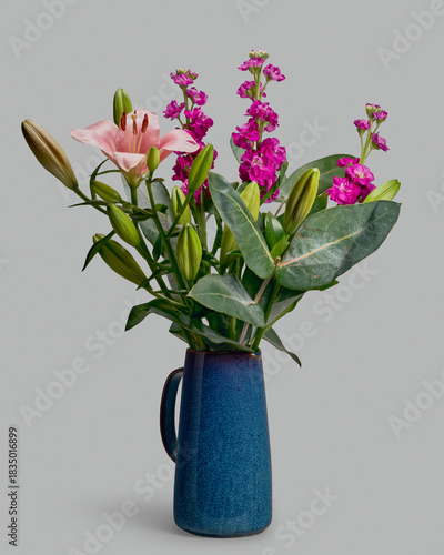 Still life of lily, eucalyptus, and levkoje bouquet in blue pitcher on gray background
