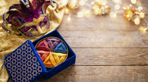 Purim holiday greeting card with carnival mask, blue gift box with gold Stars of David pattern and hamentashen cookies top view with space for text
