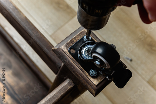 Screwing furniture wheels with brakes to a wooden table with a screwdriver.