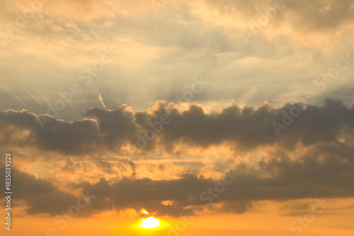 Sunbeams break dramatically through dense clouds in the orange sky.