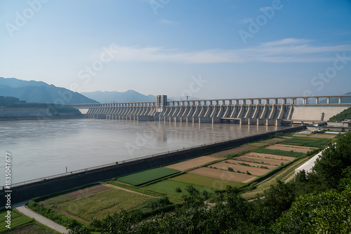 The colossal three gorges dam spanning the yangtze river, with agricultural fields under a clear sky