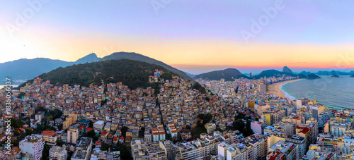 Aerial view of vibrant favelas cascading down lush green hills meet the modern city and golden sands under a pastel dawn sky, Rio de Janeiro, Brazil.