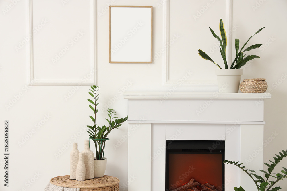 Fototapeta premium Fireplace and houseplants near white wall in room, closeup