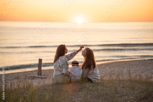 Back view of two caucasian female friends and a child enjoying sunset on the Baltic seashore. 
