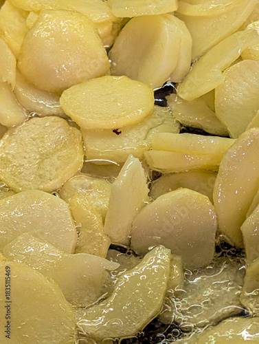 Detailed view of potato slices cooking in hot water or oil, creating a rich texture.