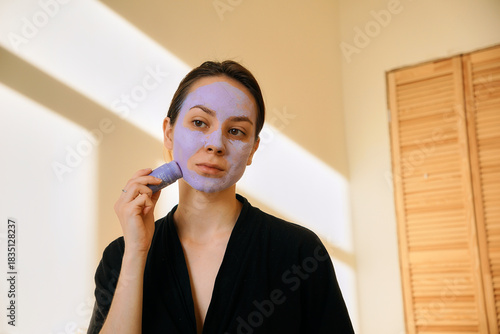 A young woman applies a clay mask in a stick to her face. Taking care of skin beauty and youth, home treatments