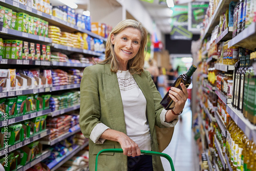 Senior woman holding bottle of olive oil while looking at camera
