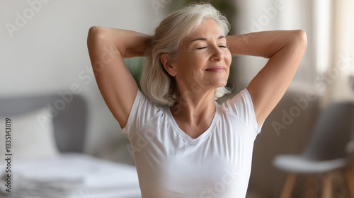 Mature woman stretching arms behind head, smiling after waking up. Happy senior female feeling refreshed, enjoying well-being, healthy lifestyle, retirement.