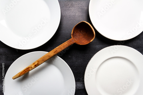 Big white plates and wooden spoon on black chalkboard background. Flat lay. Top view. Food concept. Dark mood food photography.