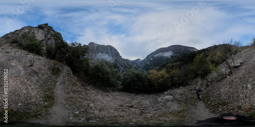 Limestone peaks nestle serene river valley in Cantabria - Serene mountain landscape features a waterfall and ancient stone bridge amidst gray and green tones.