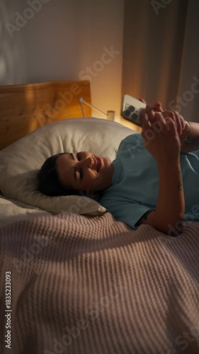relaxed female enjoys latenight phone time, young lady lounges comfortably in warm bedroom environment