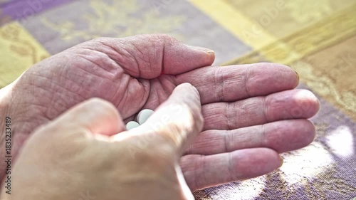A hand is holding and counting several white tablets on a table. The setting suggests an indoor space. The activity relates to health management and medication routine.