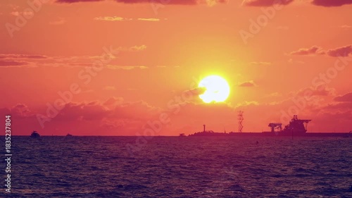 Number 2. Dramatic red-orange sunset, with the outline of coastline and ships and sailboats floating on water visible on horizon.