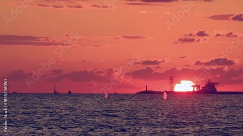 Number 7. Dramatic red-orange sunset, with the outline of coastline and ships and sailboats floating on water visible on horizon.