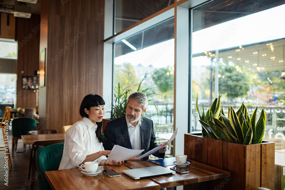 © Marko Geber - Adult woman and mature man in focused business meeting at cafe