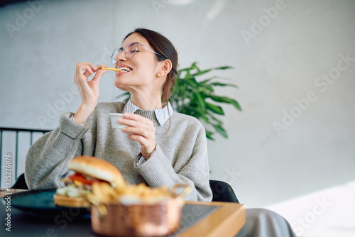 Foto Young woman with glasses eating french fries and hamburger at a modern restauran