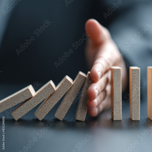 A hand halts the cascade of tumbling dominos, symbolizing effective change management, risk reduction strategies, decisive leadership actions, and smooth organizational transformation.