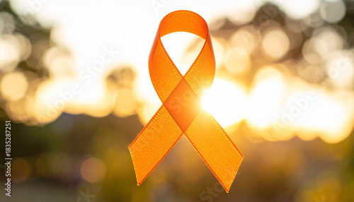 Orange awareness ribbon against a blurred background of sunlight and trees orange ribbon