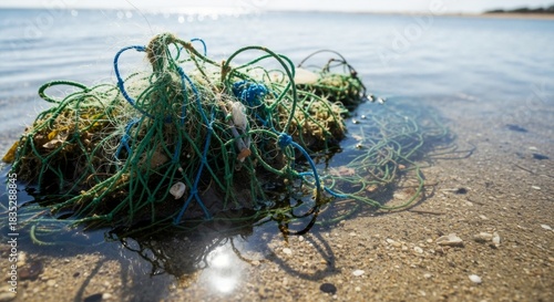 An abandoned fishing net washed up in shallow water on a sandy beach. Discarded ghost net representing plastic pollution and marine debris. Environmental conservation and ecology concept