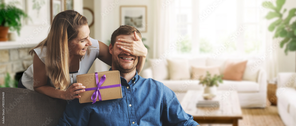 © ronstik - woman giving surprise gift to beloved man at home. closed eyes with hand from behind. banner with copy space