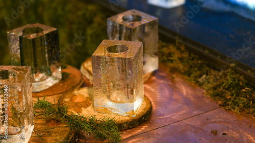 Clear ice blocks rest on circular wooden bases, surrounded by moss in a rustic, natural setting. Perfect for winter drinks. Festive shopping at a christmas market