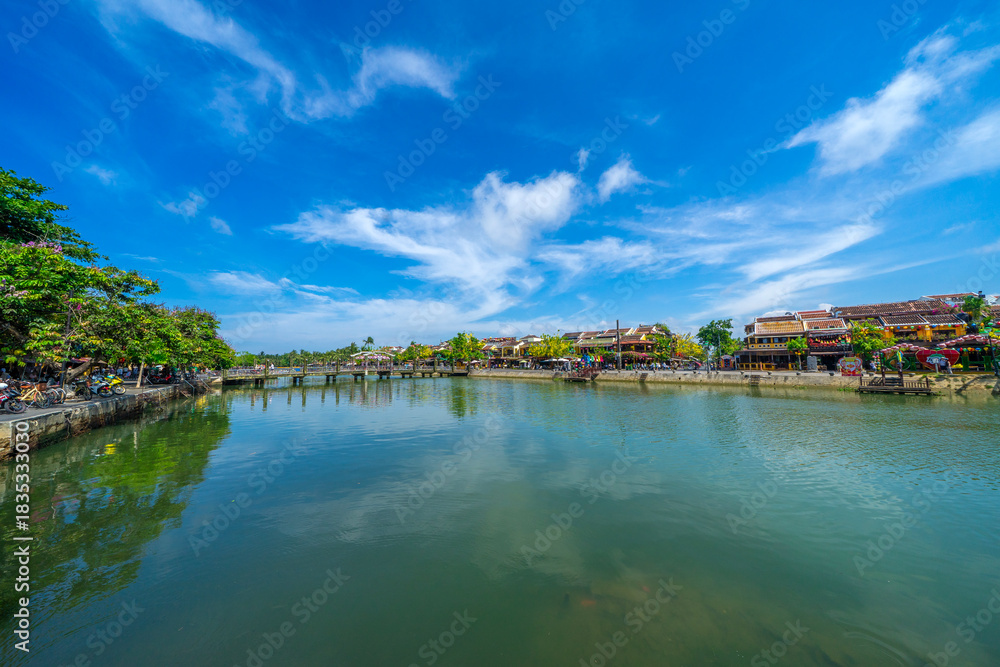 Fototapeta premium Wooden boats on the Thu Bon river in Hoi An ancient town. Yellow old houses on waterfront reflected in river. Hoi An is a UNESCO world heritage site in Vietnam