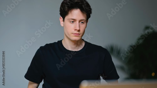 Young man stress frustration concentration furrowed brow folded hands indoor table casual clothing short hair stressed young man sits table with furrowed brow and folded hands showing frustration