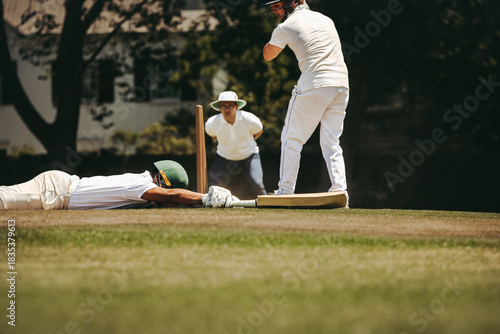 Cricket player diving to make the crease as umpire observes play